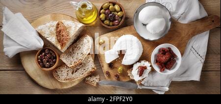 Käseplatte mit Ricotta und Mozzarella scamorza, Brot, getrockneten Tomaten, Oliven und nativem Olivenöl extra auf Holzboden. Italienische Spezialität Stockfoto