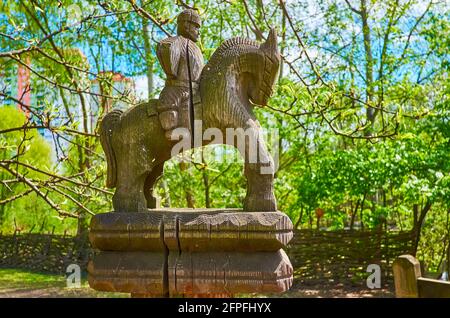 Die Vintage geschnitzte Holzskulptur des Reiters auf der Säule des Wickels gegen den grünen Garten, Mamajeva Sloboda Kosakendorf, Kiew, Ukra Stockfoto