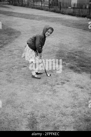 1962, historisch, ein kleines Mädchen in einem Kleid und Anorak, Golf auf einem Putting Course am Meer, Littlehampton, West Sussex, England, Großbritannien. Stockfoto