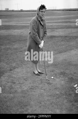 1962, historisch, eine Dame im langen Mantel beim Golfspielen, am Meer Putting Green oder Putting Course, West Green, Littlehampton, West Sussex, England, VEREINIGTES KÖNIGREICH. Stockfoto