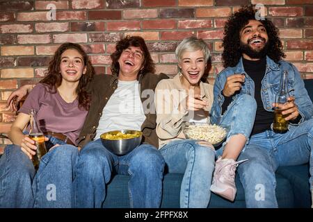 Portrait von entspannten, vielfältigen Freunden fröhlich lachend, während sie lustige Komödie im Fernsehen, Toothy Smile und Snacks während des Films anschauen Stockfoto