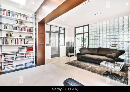 Gemütliches Interieur Design der geräumigen Hausbibliothek mit komfortablem Sofa Und Teppich in der Nähe von Bücherregalen in modernen Wohnung Stockfoto