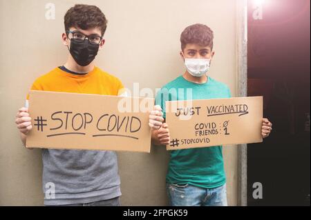 Zwei Freunde mit Masken zeigen zwei Schilder mit der Meldung STOP covid, gerade geimpft. Um das Konzept zu unterstreichen, erhalten die Freunde 1 Covid 0. Konzept o Stockfoto