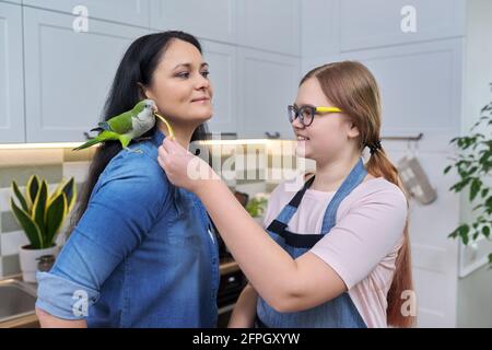 Freundliche fröhliche Familie, Porträt von Mutter und Tochter im Teenageralter, mit grünem Papagei Stockfoto