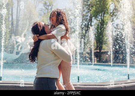 Junge Mutter und ihre Tochter haben Spaß am Brunnen im Sommerpark. Frau hält Mädchen. Familie lacht, Spiele spielen Stockfoto