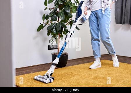 Beschnittene Frau, die mit einem Staubsauger über den Teppich im Wohnzimmer läuft, zu Hause, aufgeräumt, Haushaltsführung, Nahaufnahme, Seitenansicht Stockfoto