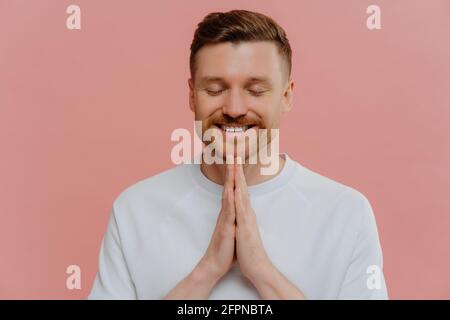 Junger glücklicher Mann mit geschlossenen Augen, der betet und bittet Etwas Stockfoto