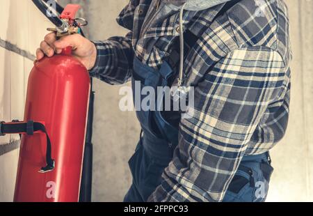 Installation des roten Feuerlöschers im Geschäftsgebäude durch einen professionellen Brandschutzmitarbeiter. Nahaufnahme. Stockfoto