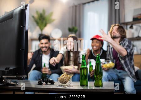 Emotionale Männer und Frauen, die während der Meisterschaft die Punktzahl der Lieblings-Fußballmannschaft feiern, mit fünf Punkten. Multiethnische Freunde sitzen auf der Couch und sehen sich ein Match im Fernsehen an. Stockfoto
