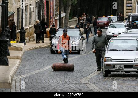 ASERBAIDSCHAN, BAKU - 2009. November: Ein uniformierte Arbeiter rollt mit dem Fuß eine Gasflasche entlang des Straßenhügels. Stockfoto