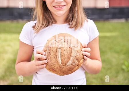 Das Kind hält ein rundes Brot. Gesunde Ernährung. Großes frisches Bäckerbrötchen tragen Stockfoto