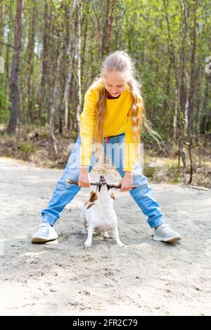 Ein Teenager-Mädchen mit langen blonden Haaren spielt mit einem Stock mit einem Hund im Park. Stockfoto