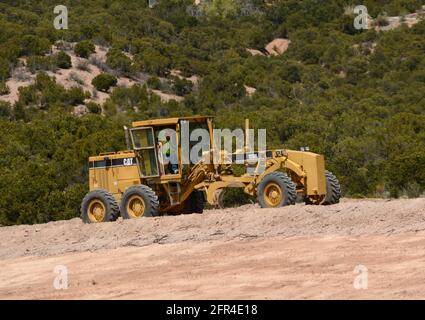 Ein Betreiber schwerer Geräte verwendet einen Caterpillar 120H Motor Grader, um Schmutz auf einer Baustelle für Straßenverbesserungen in New Mexico zu transportieren. Stockfoto