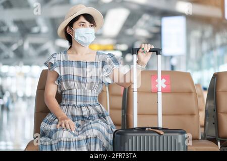 Junge Frau trägt chirurgische Gesichtsmaske im Flughafen-Terminal, Schutz Coronavirus-Krankheit (Covid-19) Infektion, asiatische Frau Reisende sitzt auf Chai Stockfoto