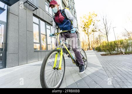 Ein junger Kurier liefert Essen mit einem gelben Thermalrucksack und fährt mit dem Fahrrad in der Stadt. Konzept für den Lieferservice von Lebensmitteln Stockfoto