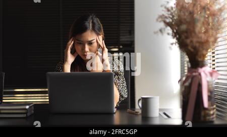 Porträt einer Geschäftsfrau, die sich während der Arbeit mit einem Laptop in gestresst fühlt Büroraum Stockfoto