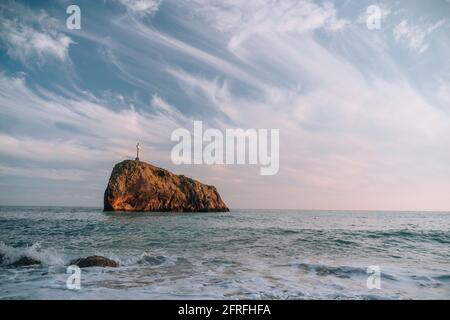 Heller Sonnenuntergang am Meer. Die Wellen stürzen in den Felsen, erleuchtet von dem warmen Sonnenuntergang, Sand und Kieselsteinen, vulkanischem Basalt wie in Island. Meereswelle bricht in Stockfoto