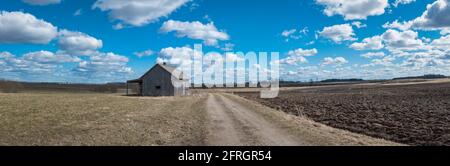 Ein altes verlassene kleines Holzhaus in den Feldern Himmel Wolken, neben einem Pfad Scheune oder gruseliges Konzept.Panoramablick. Stockfoto