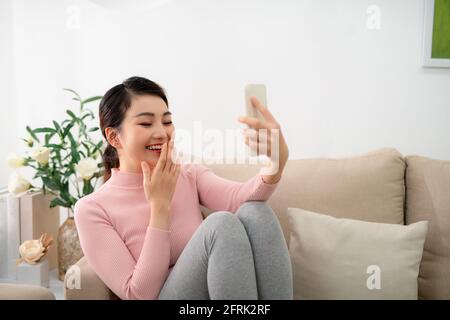 Glückliche junge Frau sitzen auf dem Sofa, halten Telefon Blick auf Bildschirm winkende Hand Video Anruf Distanz Freund Stockfoto