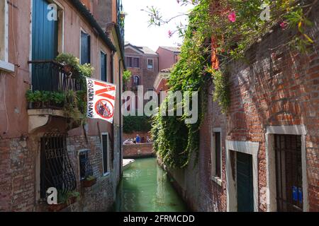 Typische venezianische Straße mit Kanal und Touristen. Poster auf dem Balkon, auf dem steht, dass es keine großen Schiffe gibt. Der Protest der Anwohner gegen Kreuzschiffe in der Stadt Stockfoto