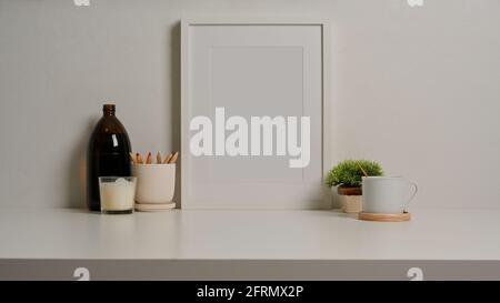 Nahaufnahme des weißen Schreibtisches mit imitiertem Rahmen, Papeterie, Tasse, Dekorationen und Kopierfläche Stockfoto