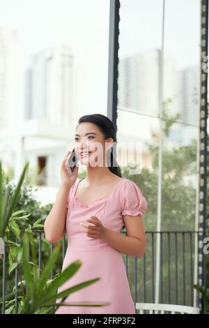 Porträt einer fröhlichen jungen Frau, die auf dem Balkon steht und telefoniert Stockfoto