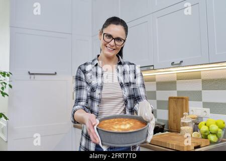 Lächelnde Frau in der Küche Fäustlinge mit heißen frisch gebackenen Kuchen Stockfoto