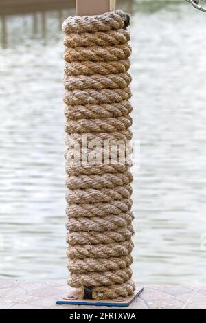 Viele Schichten Seil um einen Holzbalken gebunden, im Schatten an einem sonnigen Tag am Flussufer Stockfoto