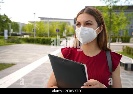 Portrait von schönen Mädchen mit FFP2 KN95 Gesichtsmaske halten Ordner, die im Freien zur Seite schauen Stockfoto