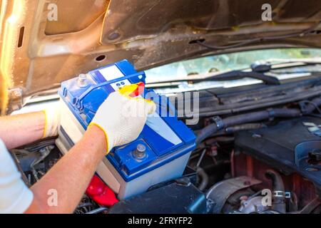 Wartung der Maschine. Ein männlicher Automechaniker nimmt eine Batterie unter der Motorhaube eines Autos heraus, um sie zu reparieren, aufzuladen oder zu ersetzen. Stockfoto