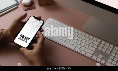 Zugeschnittenes Bild von männlichen Händen, die das Smartphone mit auf den Arbeitstisch halten Computergeräte Stockfoto
