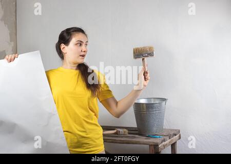 Eine Reparaturfrau klebt weiße Tapeten an die Wand. Reparaturarbeiten, Tapezieren. Platz für Textkopie. Stockfoto