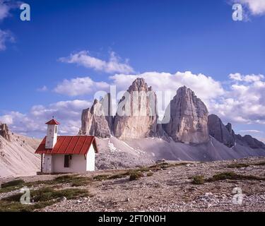 Italien. Das Bild zeigt die Kletterkapelle auf der drei Zinnen Hütte [Rifugio Locatelli], die auf die berühmten drei Türme blickt, die auf Deutsch drei Zinnen heißen, aber auf Italienisch poetischer Weise als die drei Zinnen di Laverado in der östlichen Region der italienischen Dolomiten in Sexten-Sexten genannt werden. Während des Ersten Weltkriegs, bekannt als der Weiße Krieg, stellten die Gipfel eine natürliche Barriere zwischen den Italienern und den streikenden Österreichern dar, wobei die Front durch die Gipfel lief. Stockfoto