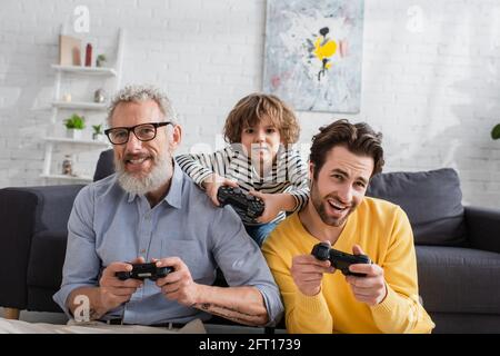 KIEW, UKRAINE - 12. APRIL 2021: Lächelnde Männer und Jungen mit Joysticks zu Hause Stockfoto