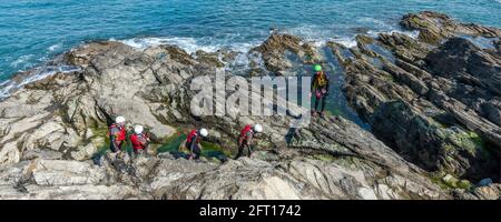 Ein Panoramabild von Urlaubern und ihrem Fremdenführer, die auf einem koolenkenden Abenteuer auf Towan Head in Newquay in Cornwall über Felsen wandern. Stockfoto