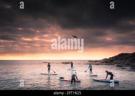 Eine Gruppe von Urlaubern paddeln auf Stand Up Paddleboards, während die Sonne über der Fistral Bay in Newquay in Cornwall untergeht. Stockfoto