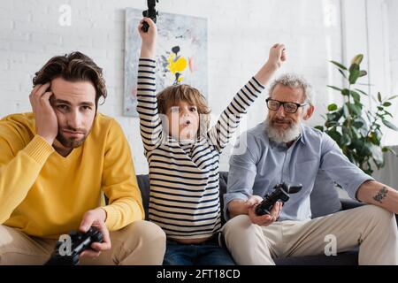 KIEW, UKRAINE - 12. APRIL 2021: Kind zeigt Ja-Geste bei traurigen Eltern mit Joysticks Stockfoto