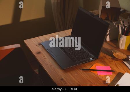 Das Home Office, ein Beispiel für einen Raum für Telearbeit von zu Hause aus, in dem Sie einen schwarzen Laptop und einige farbige Notizen, früh am Morgen, in sehen können Stockfoto