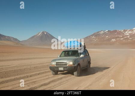 Vor dem Hintergrund von Vulkanen fährt ein Geländewagen im Geländewagen auf einer Touristensafari über Land durch die Wüstenlandschaft Boliviens. Stockfoto