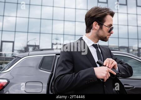 Bärtiger Bodyguard in Sonnenbrille und Anzug mit Pistole fast modern Gebäude Stockfoto