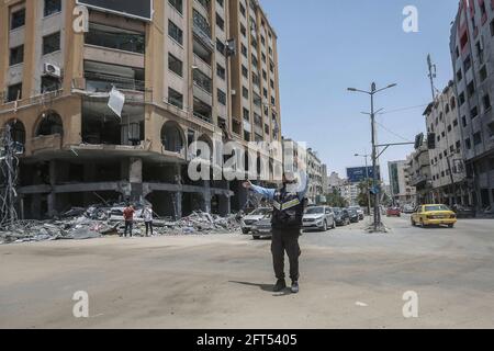 Gaza-Stadt, Palästinensische Gebiete. Mai 2021. Ein Verkehrspolizist steht in der Nähe eines der zerstörten Türme und regelt den Verkehr. Israel und die Hamas haben nach tagelangen Kämpfen, bei denen etwa 230 Palästinenser bei israelischen Luftangriffen getötet und 12 Menschen in Israel durch Raketenbeschuss aus dem Gazastreifen getötet wurden, eine Einigung über den Waffenstillstand erzielt. Kredit: Mohammed Talatene/dpa/Alamy Live Nachrichten Stockfoto