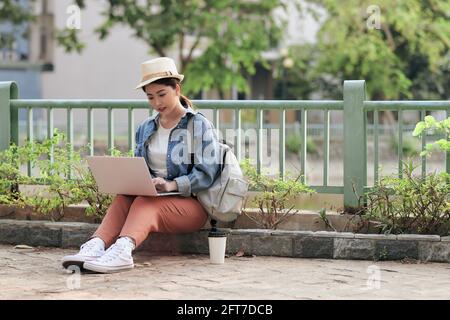 Konzentriert bei der Arbeit. Selbstbewusste junge asiatische Frau trägt lässig und arbeitet auf Laptop für Remote-Learning von überall zu tun, während auf der CI sitzen Stockfoto