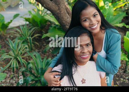 Porträt einer afroamerikanischen Mutter mit Tochter im Garten, lächelnd und umarmend. Familie genießt die Zeit im Freien, Lifestyle-Konzept. Stockfoto