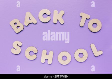 Inschrift ZURÜCK ZUR SCHULE aus Holzbuchstaben auf violettem Hintergrund. Das Konzept der Bedeutung von Bildung. Stockfoto
