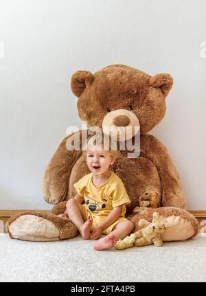 Süßer, fröhlicher Junge, der mit seinem riesigen Teddybären spielt, drinnen zu Hause Stockfoto