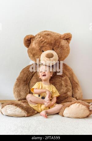 Süßer, fröhlicher Junge, der mit seinem riesigen Teddybären spielt, drinnen zu Hause Stockfoto