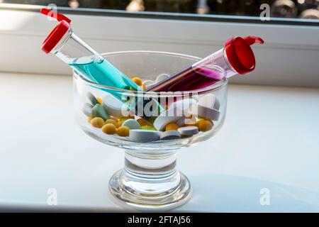 Gelbe, weiße, grüne Tabletten und zwei Reagenzgläser mit roter und blauer Flüssigkeit in einer transparenten Glasvase. Die Substanz ist ähnlich wie ein Medikament oder Vaccin Stockfoto