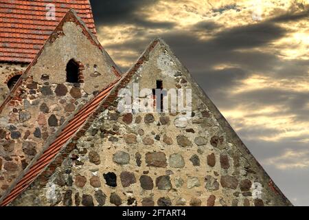 Oberer Teil der spitzen Dächer der verlassenen alten Dorfkirche in Deutschland, mit dramatischen Wolken am Himmel Stockfoto