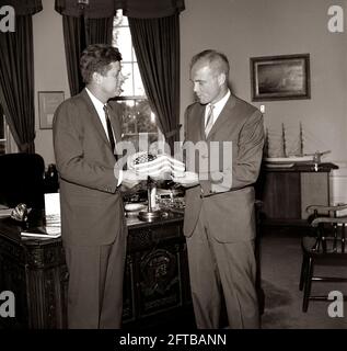 Präsident John F. Kennedy erhält vom Astronauten-Oberstleutnant John H. Glenn, Jr. (rechts) ein Geschenk einer amerikanischen Flagge; LT. Col. Glenn trug die Flagge in seinem Raumanzug während seines Orbitalfluges an Bord von Mercury-Atlas 6, auch bekannt als Friendship 7. Der Sonderassistent des Präsidenten, Kenneth P. O'Donnell, steht im Hintergrund. Oval Office, White House, Washington, D.C. Stockfoto