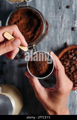 Blick aus der Höhe auf einen jungen kaukasischen Mann, der den Trichter einer Mokakanne mit gemahlenem Kaffee füllte, an einem grauen rustikalen Holztisch Stockfoto